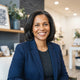 A professional portrait of a diverse woman smiling in a modern, well-lit home interior with slate blue and white decor.